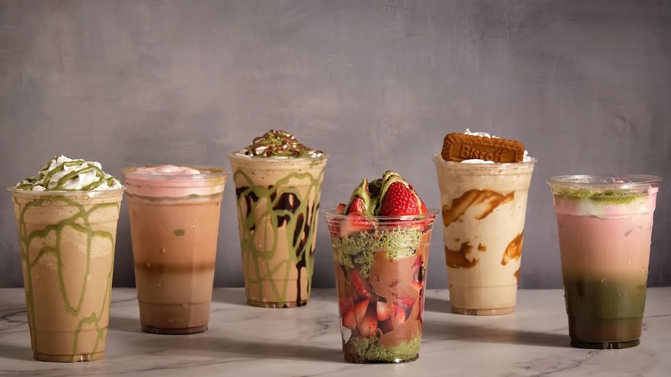 A pistachio frappe in Houston lined up with five more drinks on marble, including pistachio drizzled cups and a Biscoff frappe with a cookie on top