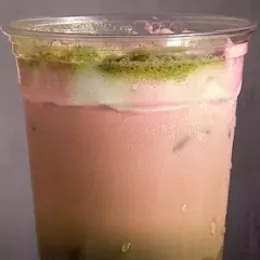 A strawberry matcha in a clear cup, a pink strawberry layer over green matcha with matcha dusted on the foam.